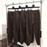 Quattro pantaloni marroni casual e eleganti su supporto minimalista in metallo italiano.