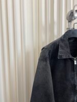 Giaccone in suede nero con zip su gruccia moderna, sfondo di pannelli neutri e dettagli eleganti.