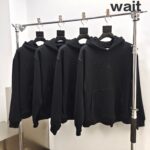 Vestiti casual neri minimalisti con scritta “Wait” su esposizione moderna e elegante.