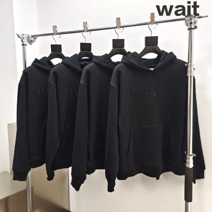 Vestiti casual neri minimalisti con scritta “Wait” su esposizione moderna e elegante.