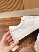Sneakers bianche moderne, minimaliste e versatili su superficie di legno naturale.