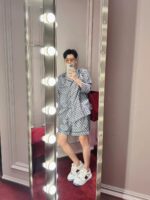 Donna con outfit casual chic davanti a uno specchio luminoso e ambiente trendy.