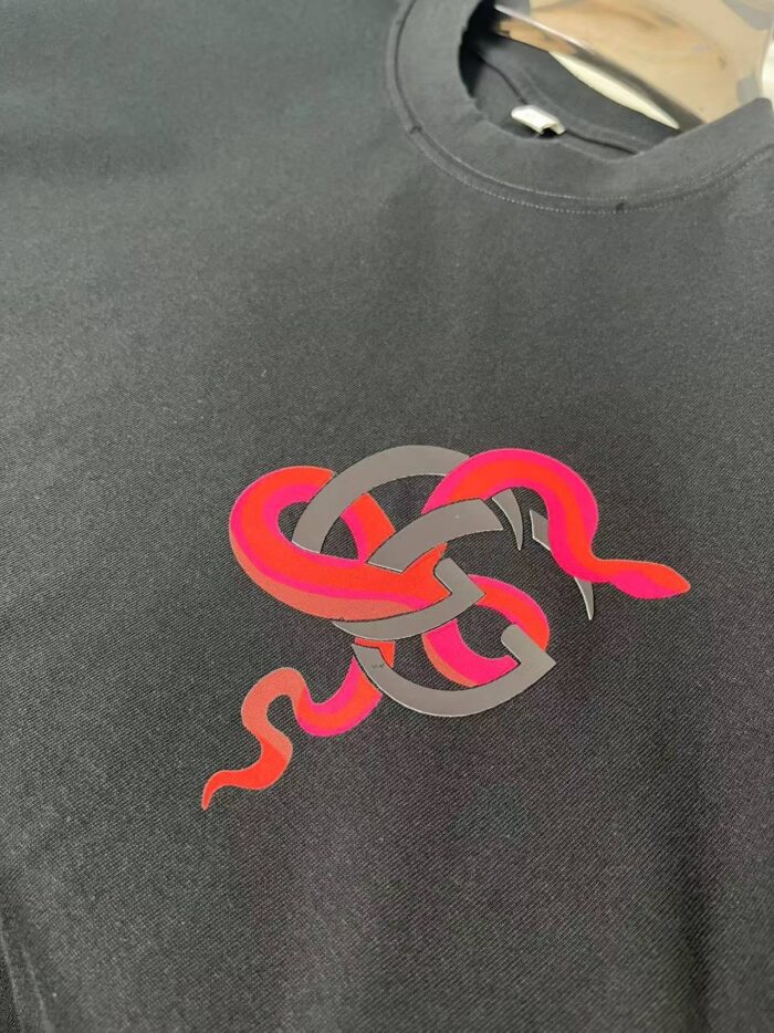 Maglietta nera con grafica di serpenti colorati e motivo a nodo centrale.