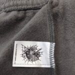 Maglione in pile grigio con etichetta ragnatela nera, stile casual e outdoor.