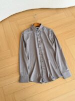 Camicia grigia a maniche lunghe in stile minimalista su pavimento in legno naturale.