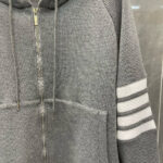 Felpa grigia con cappuccio, tasca frontale e strisce sportive bianche, stile casual e moderno.