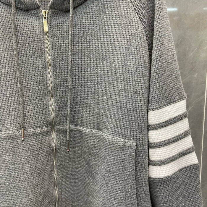 Felpa grigia con cappuccio, tasca frontale e strisce sportive bianche, stile casual e moderno.