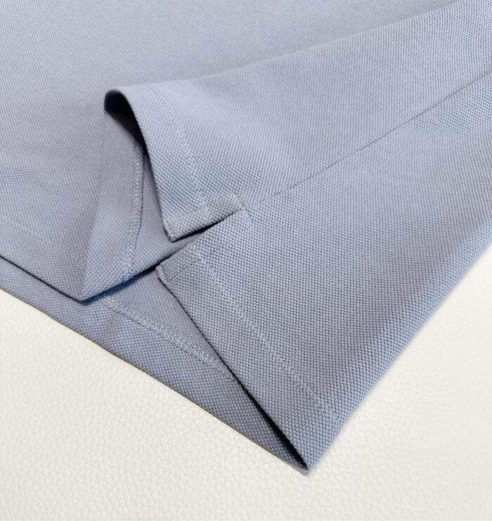 Dettaglio manica e bordo di camicia azzurro morbido e di qualità, con cuciture precise.