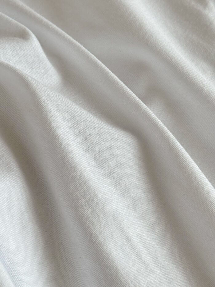 Tessuto bianco morbido con pieghe leggere e riflessi delicati, ideale per arredamento e abbigliamento.