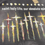 Maglietta scura con croci colorate e messaggio di fede, stile moderno e spirituale.