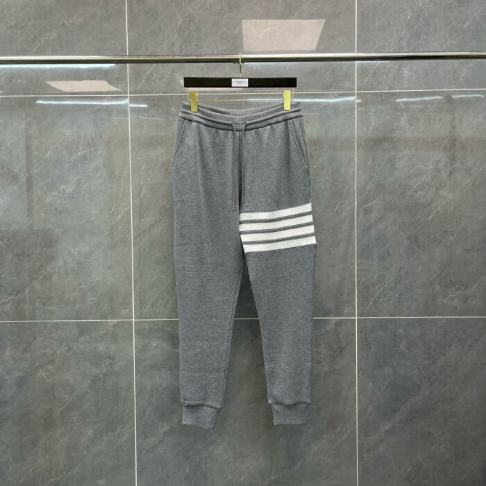 Pantaloni sportivi grigi con strisce bianche diagonali, tessuto morbido e design moderno.