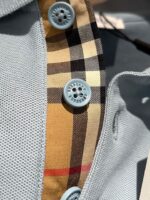 Camicia sportiva a rete grigia con dettagli a quadri beige e bottoni blu chiaro.