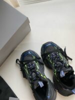 Scarpe da corsa nere con dettagli colorati, scatola semplice e accessorio sportivo, stile moderno.