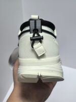 Sneaker bianco sportiva con cinturino nero, dettagli moderni e suola rialzata per stile e comfort.