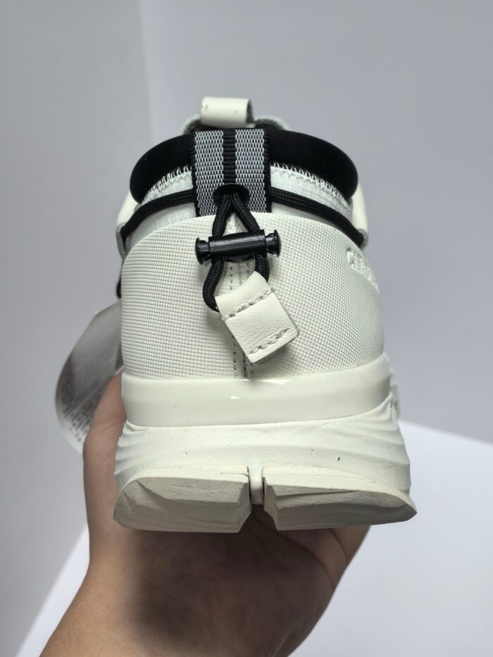 Sneaker bianco sportiva con cinturino nero, dettagli moderni e suola rialzata per stile e comfort.