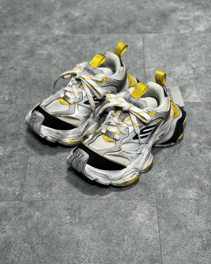 Sneaker sportiva bianca con dettagli gialli e neri, design moderno e suola robusta.