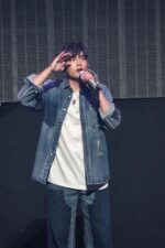 Giovane artista sul palco durante un energico concerto, stile casual e coinvolgente.