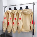 Felpe beige con logo rosso, stile streetwear, display moderna e design trendy.