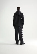 Look streetwear nero con felpa e pantaloni grafici, stile urbano e moderno.
