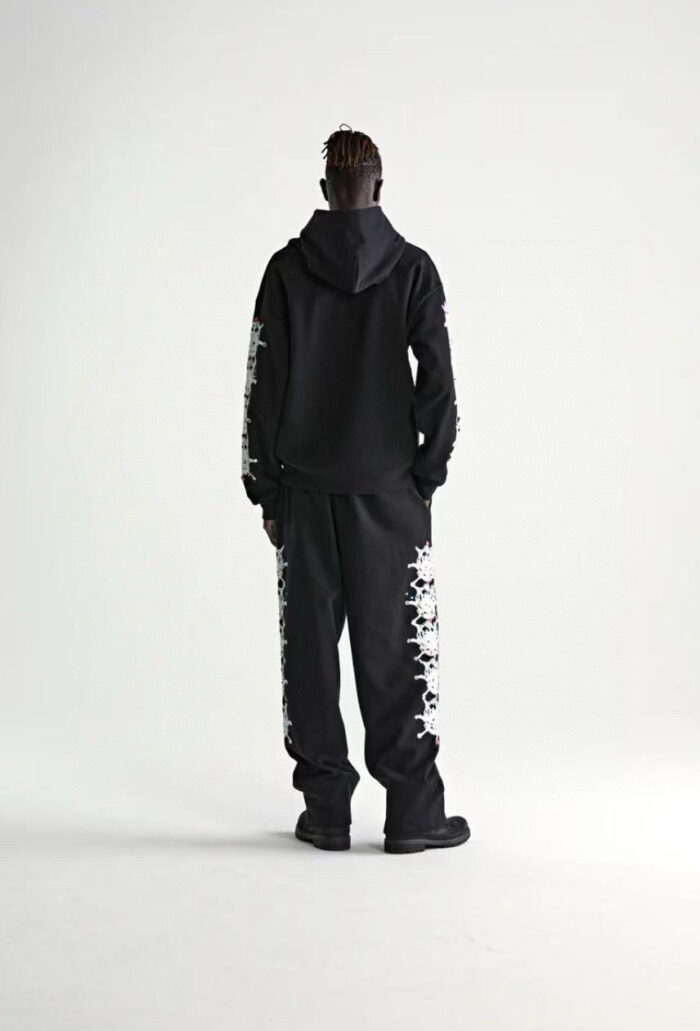 Look streetwear nero con felpa e pantaloni grafici, stile urbano e moderno.