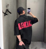 Persona che scatta un selfie con maglietta nera con logo rosso in ambiente urbano.