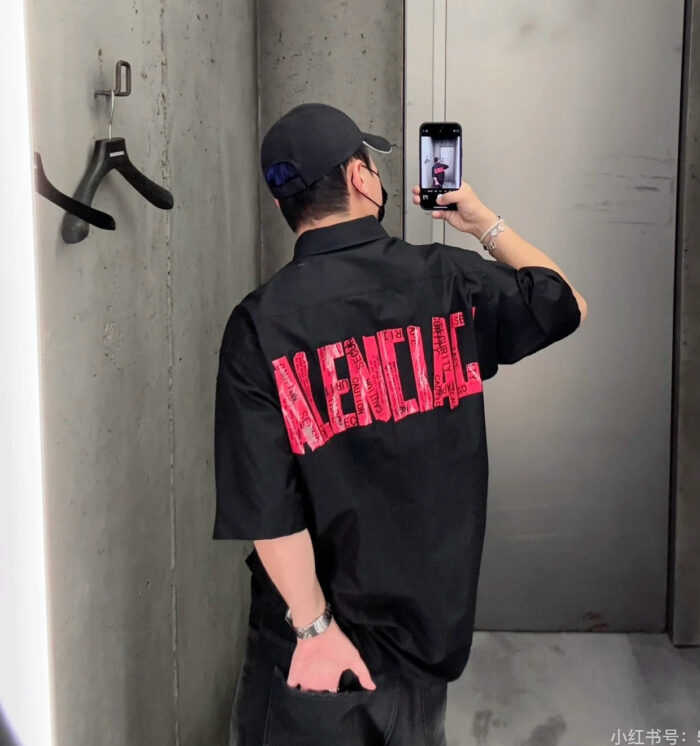 Persona che scatta un selfie con maglietta nera con logo rosso in ambiente urbano.