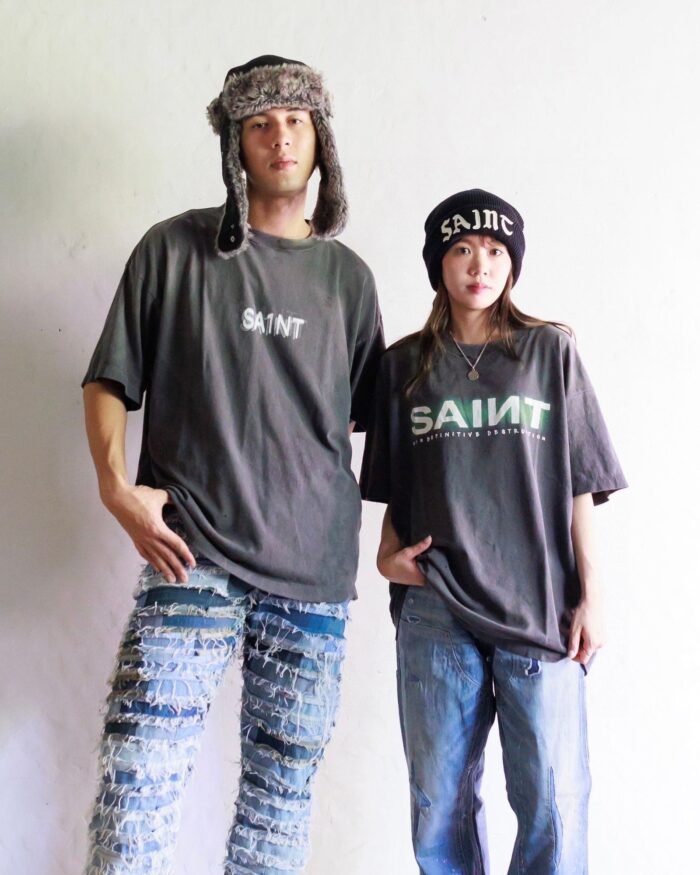 Gemelli streetwear con T-shirt Saint oversized, jeans strappati e accessori urbani in stile casual.