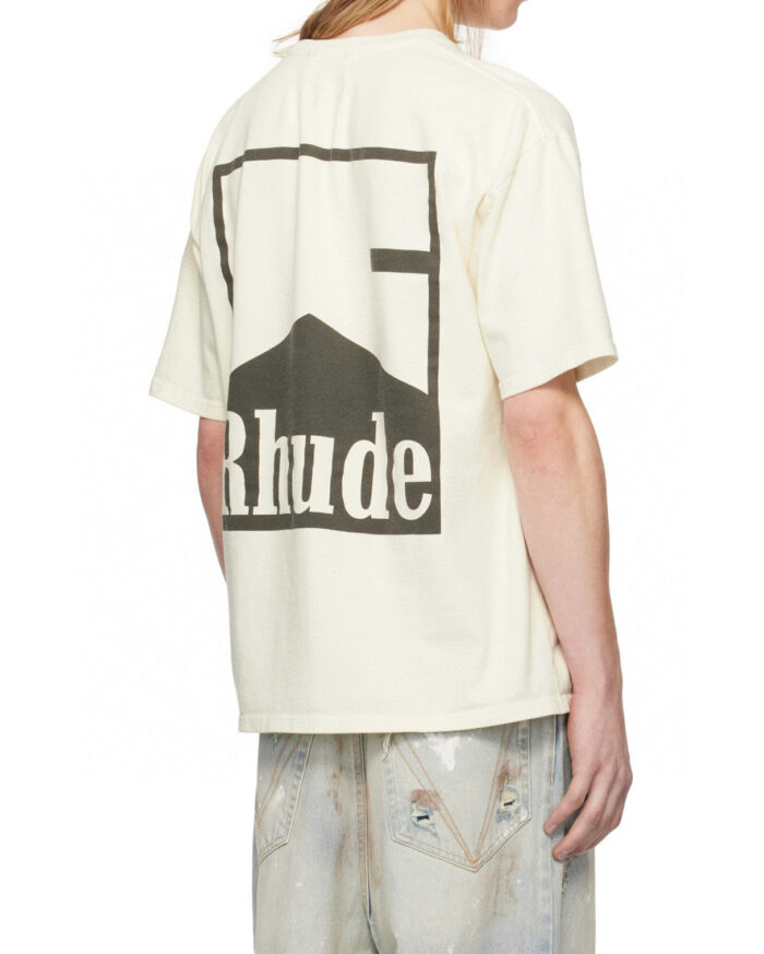 T-Shirt cream con grafica montagna e brand Rhude, abbigliamento streetwear con denim distressed.