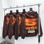 Felpe con cappuccio streetwear marroni con grafica arancione e nero, stile urbano moderno.