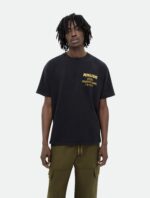 Uomo streetwear con t-shirt nera logo giallo RHUDE e pantaloni cargo oliva.