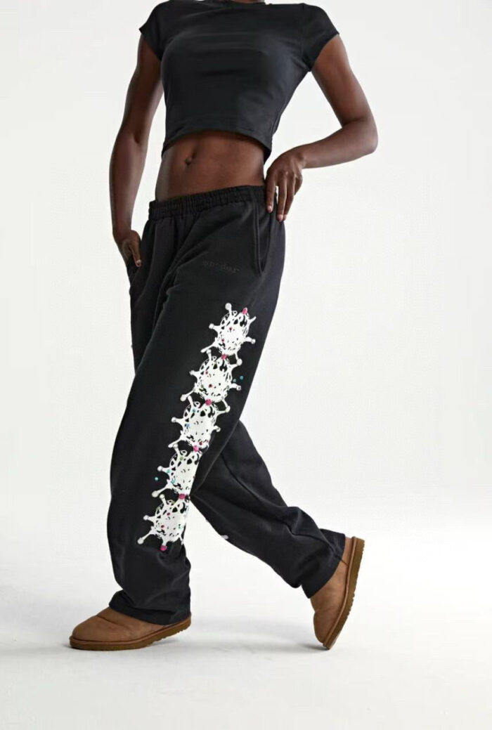 Modella in streetwear con crop top nero, joggers con teschi colorati e slip-on beige.