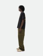 Giovane uomo streetwear con dreadlocks, maglietta nera, pantaloni oliva e sneakers beige.