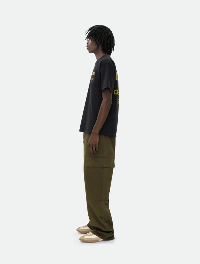 Giovane uomo streetwear con dreadlocks, maglietta nera, pantaloni oliva e sneakers beige.