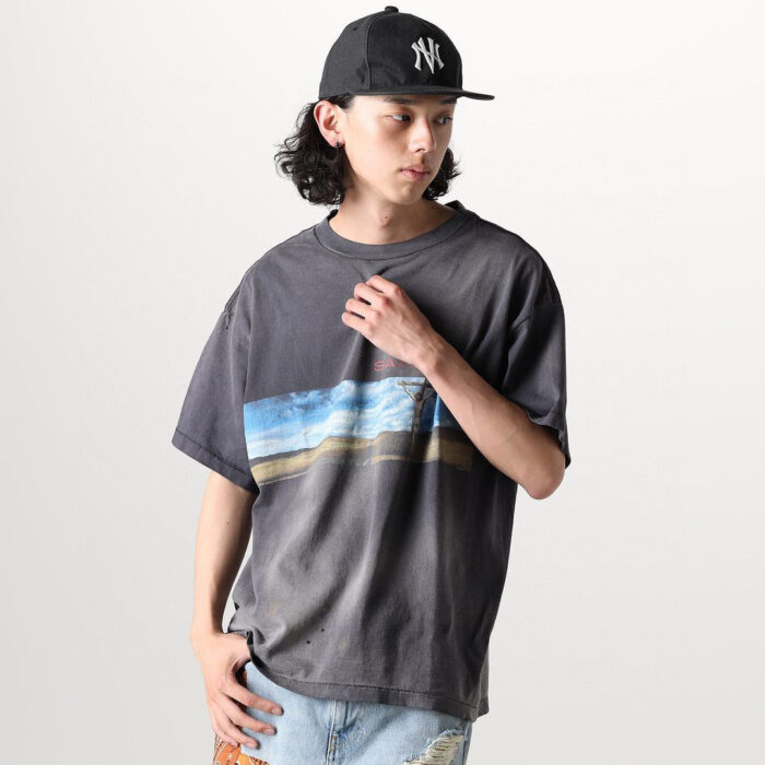 Giovane uomo streetwear con maglietta grafica paesaggistica, cappellino e jeans distressed casuale