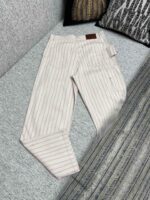 Pantaloni a righe beige casual eleganti con tasche e dettaglio in pelle su divano decorativo.