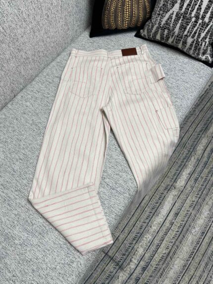 Pantaloni a righe beige casual eleganti con tasche e dettaglio in pelle su divano decorativo.