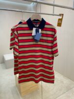 Maglietta polo a righe beige e rosso con colletto navy in ambiente moderno e minimalista.