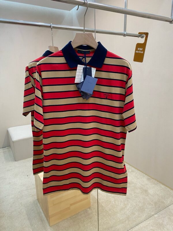 Maglietta polo a righe beige e rosso con colletto navy in ambiente moderno e minimalista.
