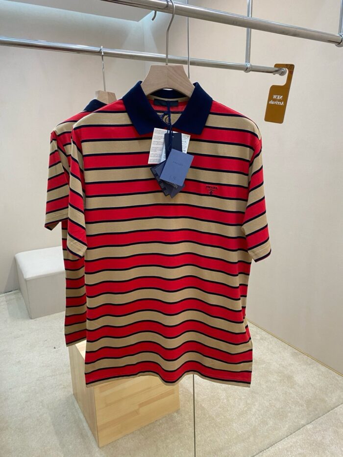 Maglietta polo a righe beige e rosso con colletto navy in ambiente moderno e minimalista.