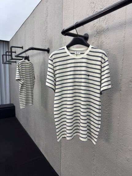 T-shirt a righe minimalista su supporto nero in showroom moderno con muro in cemento chiaro.