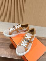 Sneaker beige e marroni con dettagli in pelle su superficie di legno con scatola arancione vibrante.