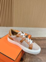 Sneaker beige con dettagli in cuoio, suola bianca, su scatola arancione, stile casual ed elegante.