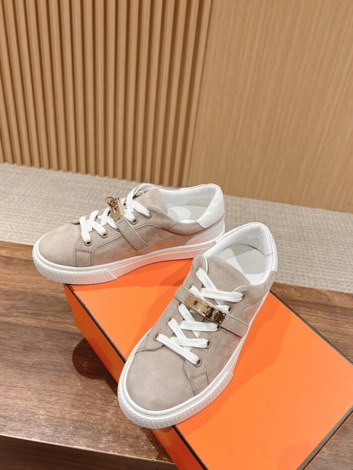 Sneakers beige eleganti con suola bianca su superficie di legno, box arancione e sfondo minimalista.