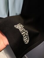 Manica nera con logo ricamato, stile moderno, tessuto elegante, sfondo azzurro chiaro.