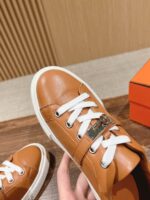 Sneaker in pelle marrone con lacci bianchi, dettaglio metallico, stile elegante e versatile.