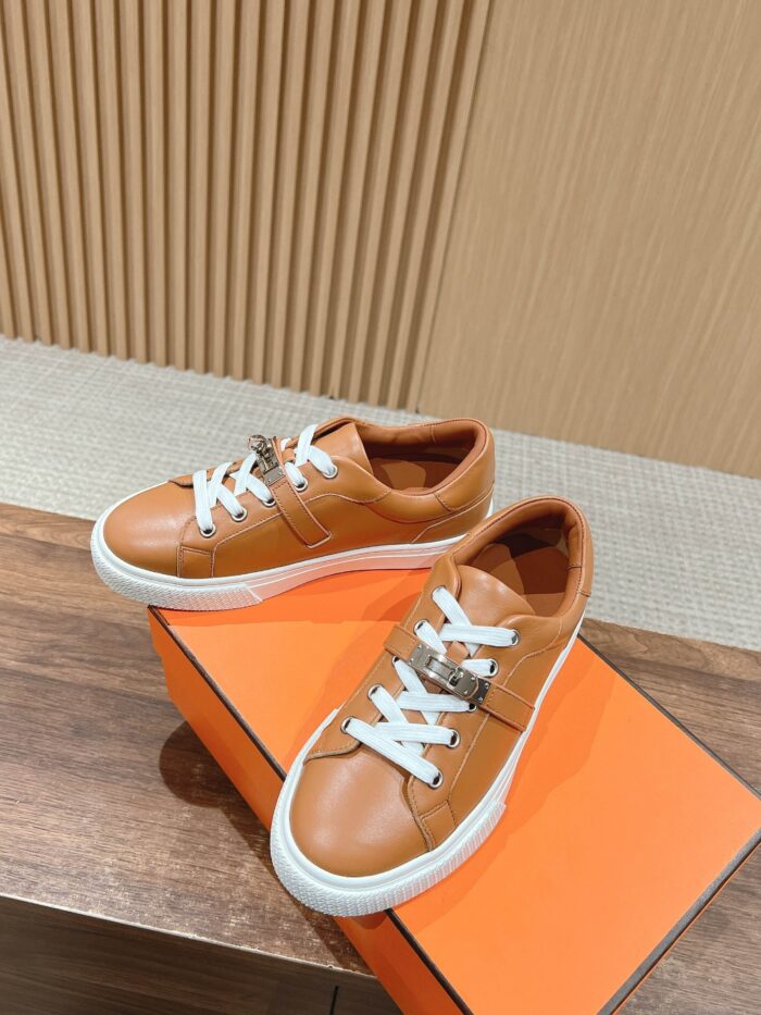 Sneakers marroni in pelle con lacci bianchi su scatola arancione, stile elegante e moderno.