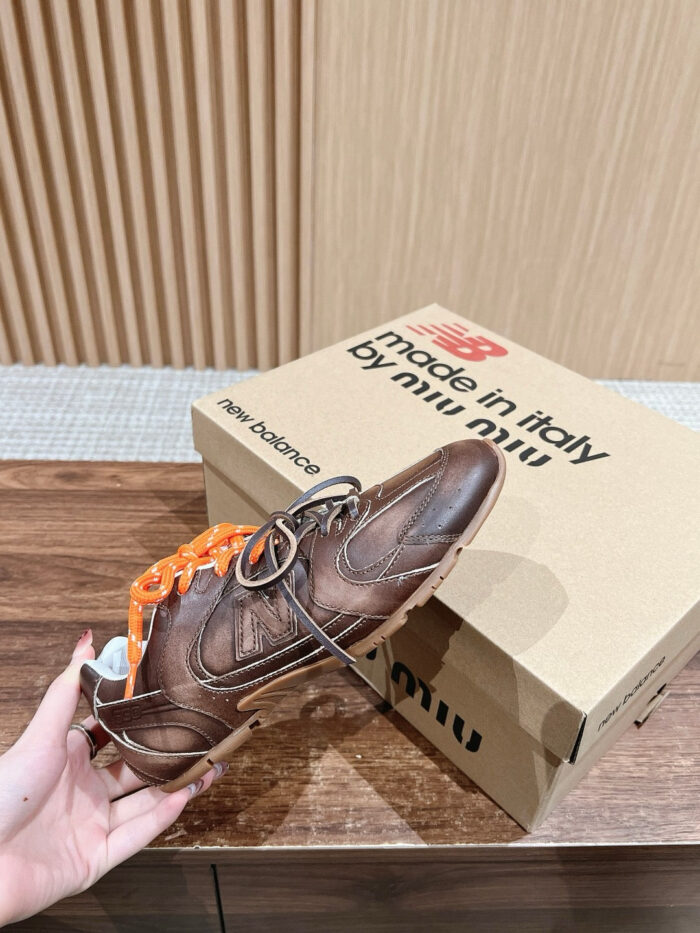 Sneaker in pelle marrone con lacci arancioni, in design elegante e moderno, su sfondo raffinato.