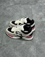 Sneaker Chanel nera e bianca con dettagli rosa, stile athleisure e logo iconico su sfondo urbano.