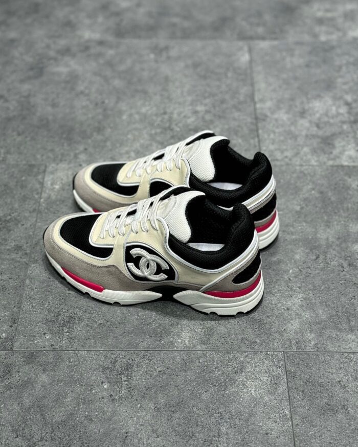 Sneaker Chanel nera e bianca con dettagli rosa, stile athleisure e logo iconico su sfondo urbano.