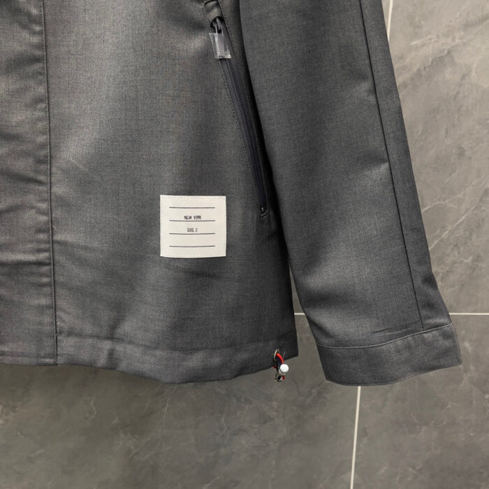 Giacca moderna grigia con tasca zip, dettaglio rosso e tag minimalista, stile sofisticato e pratico.